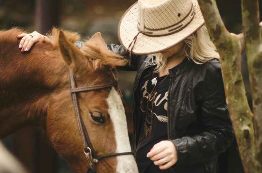a girl in a hat standing next to a brown horse