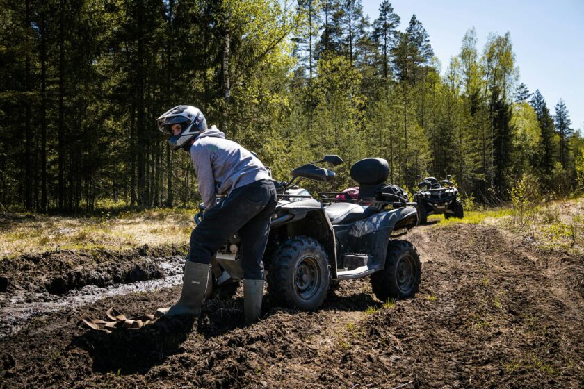 man in a helmet standing in the mud next to a quad bike